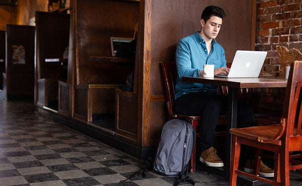 A person working on their laptop at a cafe with the Luminary 15 leaned up against their chair.
